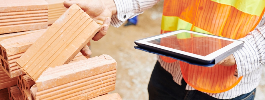 Zdjęcie przedstawia inspektora nadzoru rynku wyrobów budowlanych podczas kontroli na terenie budowy. Na zdjęciu widoczne tylko ręce inspektora. W rękach trzyma tablet.