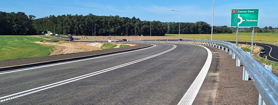 Na zdjęciu widać pustą drogę asfaltową, która łagodnie skręca w lewo. Na prawym poboczu stoi znak informujący o skręcie w prawo w kierunku Strykowa.